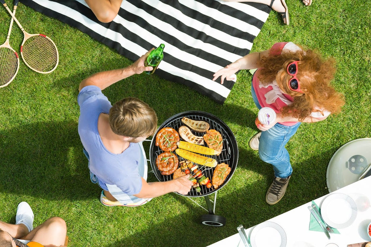 People grilling food on a barbecue grill in a grassy area.