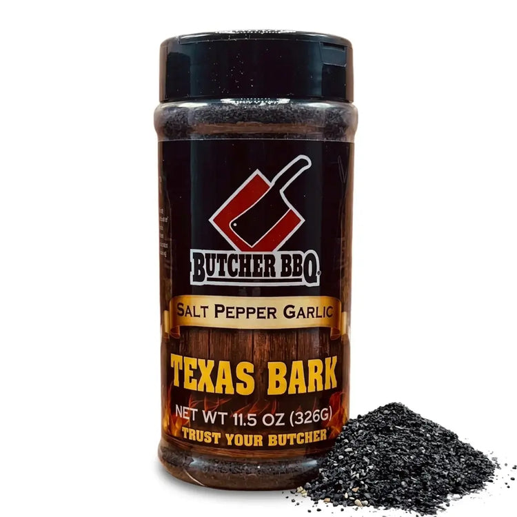 A bottle of Butcher BBQ Salt Pepper Garlic seasoning with a pile of dark Texas Bark seasoning in front, on a white background.