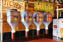Four hanging meat grinders with a rustic wooden wall and signs in the background.