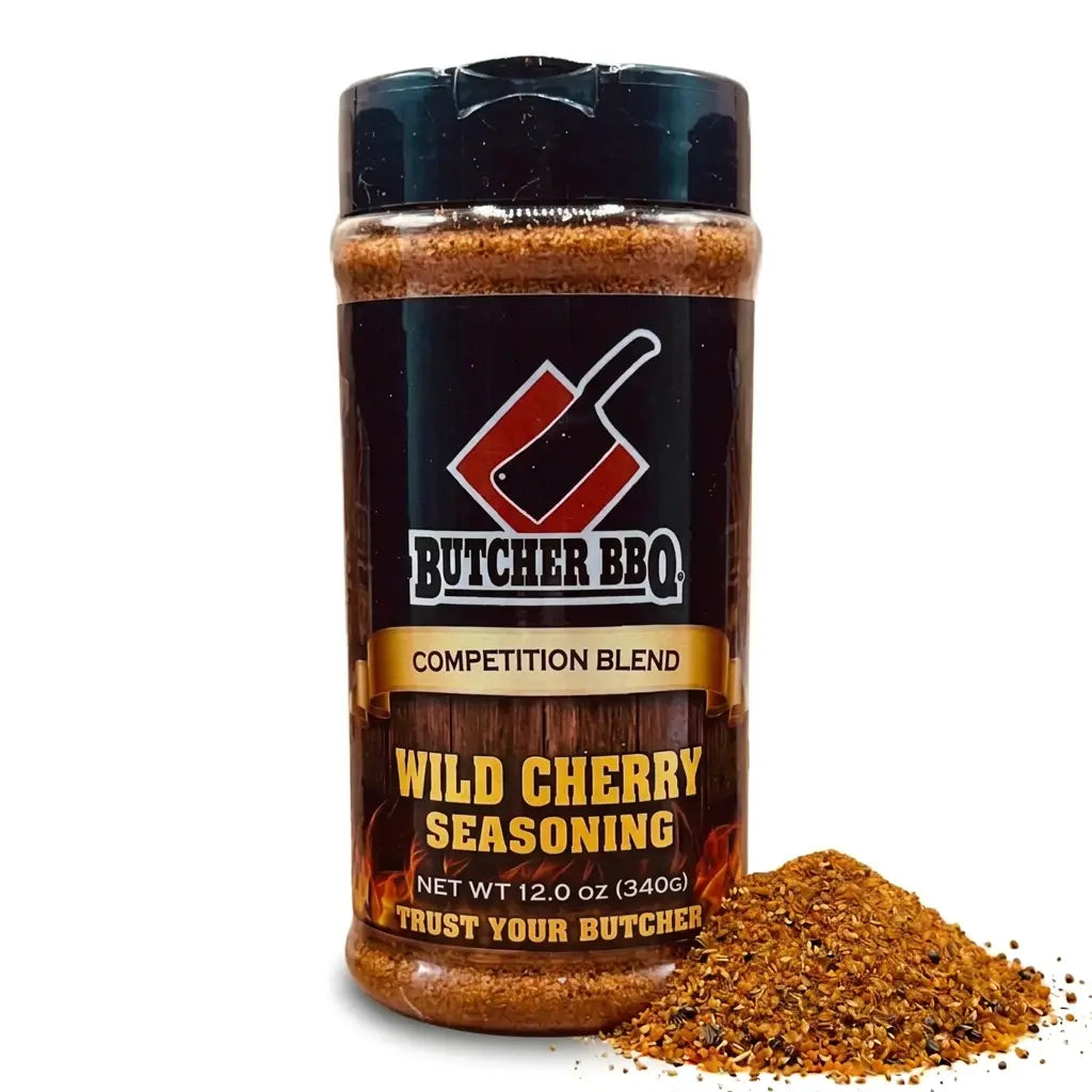 A bottle of Butcher BBQ Wild Cherry Seasoning with a black cap and a black label featuring red and gold accents, shown next to a small pile of the brown spice blend on a white background.